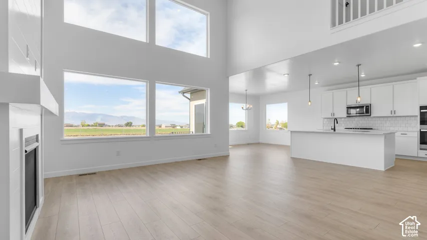 Double-height ceilings with expansive windows, wood-finish flooring, floor-to-ceiling fireplace, and kitchen featuring a center island and white cabinetry