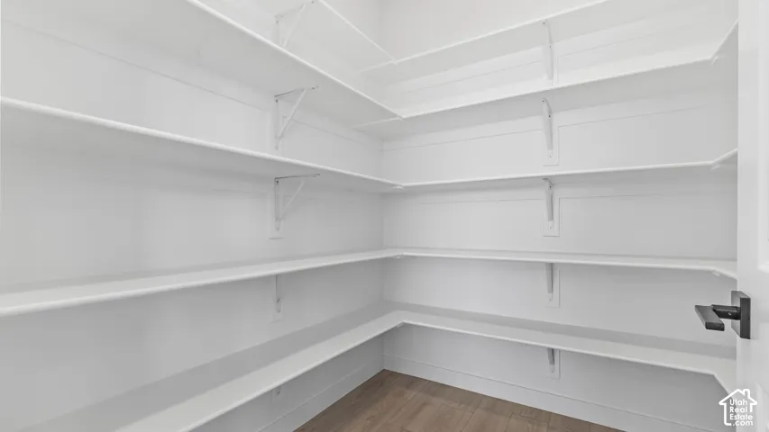 Walk-in storage space featuring multi-tiered white shelving, wood-finish flooring, and a matte black door handle