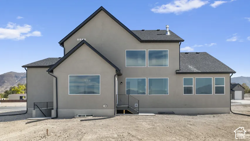 Multi-level residence featuring stucco siding, black metal roof trim, large picture windows, and metal stair railing, set against a mountain backdrop