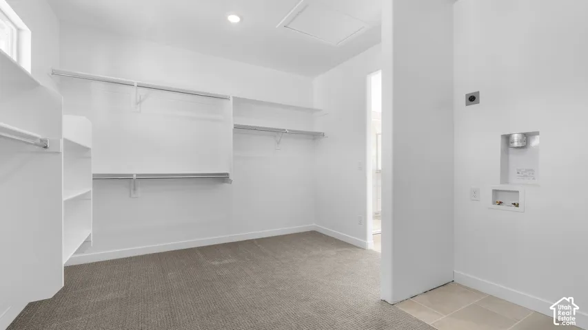 Built-in white shelving and hanging rods, neutral carpeting, recessed lighting, and dedicated laundry utility hookups with tile flooring