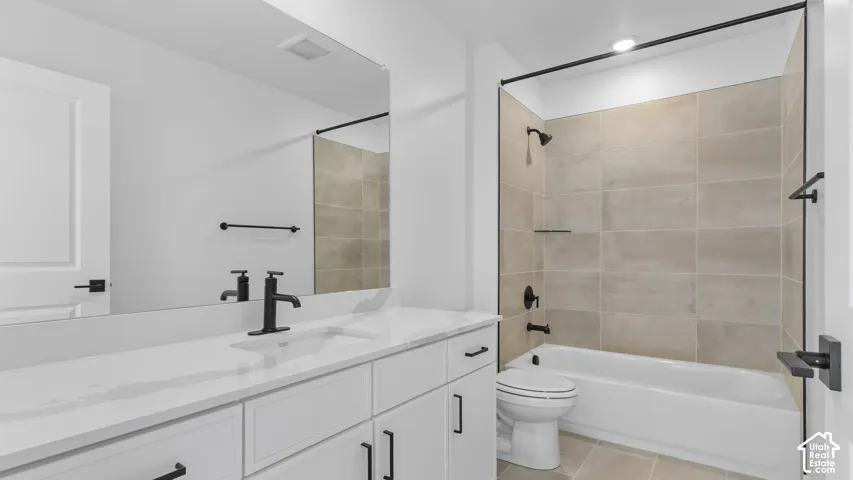 Bathroom featuring a white vanity with a solid surface countertop, rectangular undermount sink, matte black fixtures, and a shower-tub combination with large-format neutral tile surround