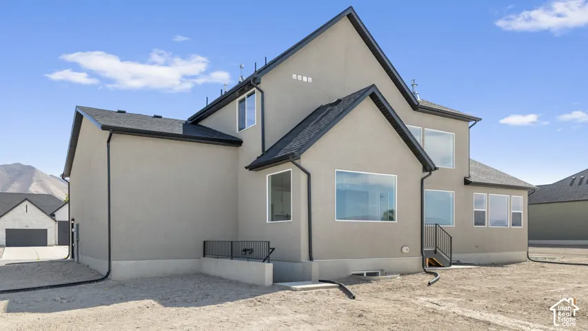 Two-story stucco exterior featuring a multi-gabled roofline, dark metal raingutters, large picture windows, and a metal perimeter railing