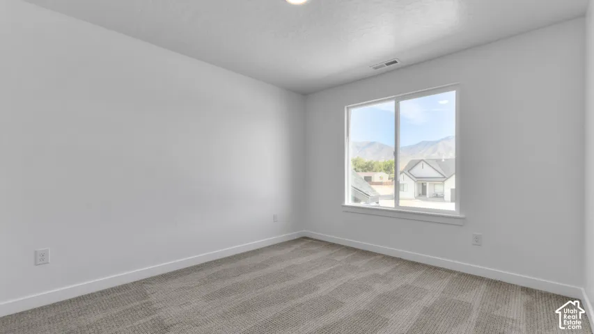Neutral-toned interior space featuring light-colored wall paint, plush carpeting, a wide window with mountain scenery, and crisp white window casing