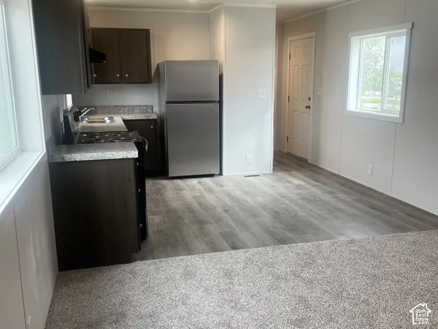 Kitchen featuring dark-finish cabinetry, stone-patterned countertops, stainless steel refrigerator, and wood-finish flooring
