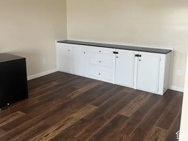 Built-in white cabinetry featuring a dark countertop, three central drawers, and dual-door storage compartments, complemented by wood-finish flooring