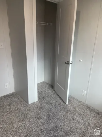 Neutral-toned carpet flooring, panel walls, and a closet with a built-in shelf and rod featuring a paneled door with brushed-nickel hardware