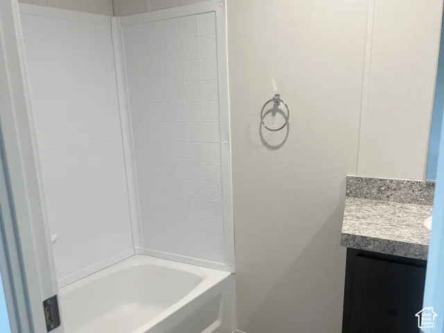 Full-size tub with integrated white shower surround, vanity with stone-patterned countertop, and circular metal towel ring