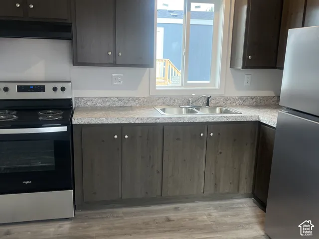 Kitchen featuring dark wood-finish cabinetry, stone-patterned laminate countertops, stainless steel appliances, a dual-basin stainless steel sink, and wood-finish flooring