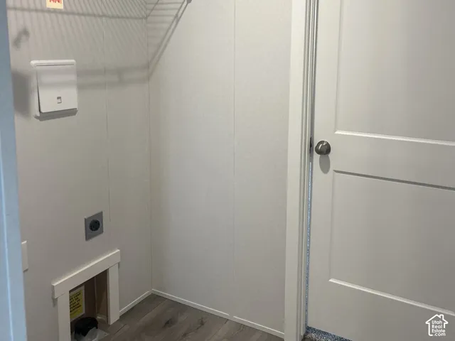 Utility space featuring wood-finish flooring, a two-panel interior door with brushed nickel hardware, built-in wire shelving, and recessed wall plumbing connections
