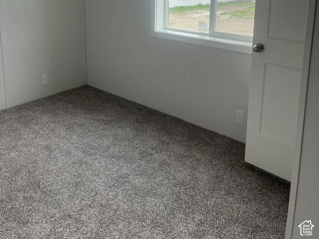 Bedroom 3 featuring neutral wall finishes, grey textured carpeting, a sliding window with white trim, and a multi-panel interior door with a brushed nickel knob