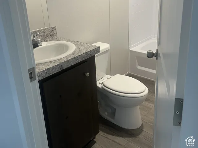 Guest Bathroom featuring wood-finish flooring, a vanity with a patterned countertop, integrated basin, and a tub-shower combination with a surround