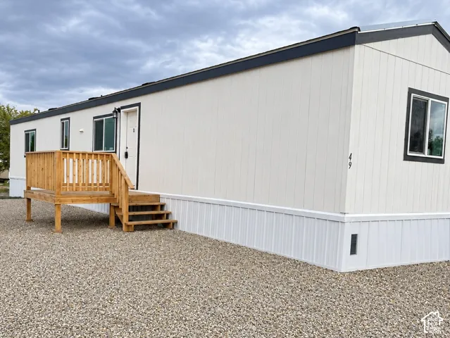 Exterior featuring vertical siding, dark trim, a wooden deck with railing, and gravel ground cover