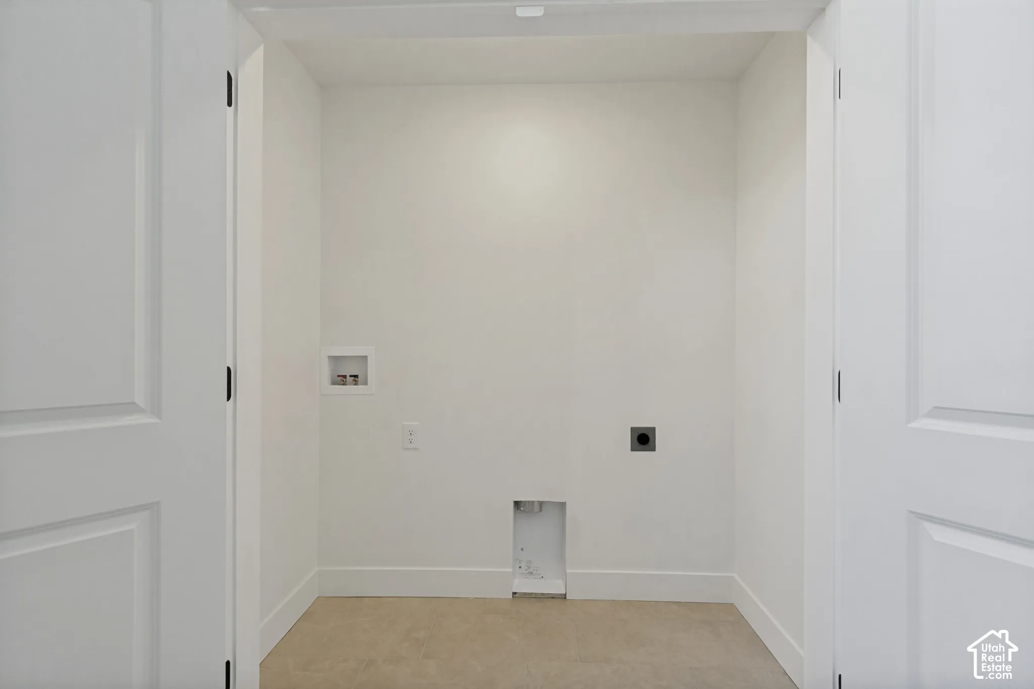 Dedicated utility alcove featuring dual paneled swing doors, neutral tile flooring, and integrated plumbing and electrical hookups