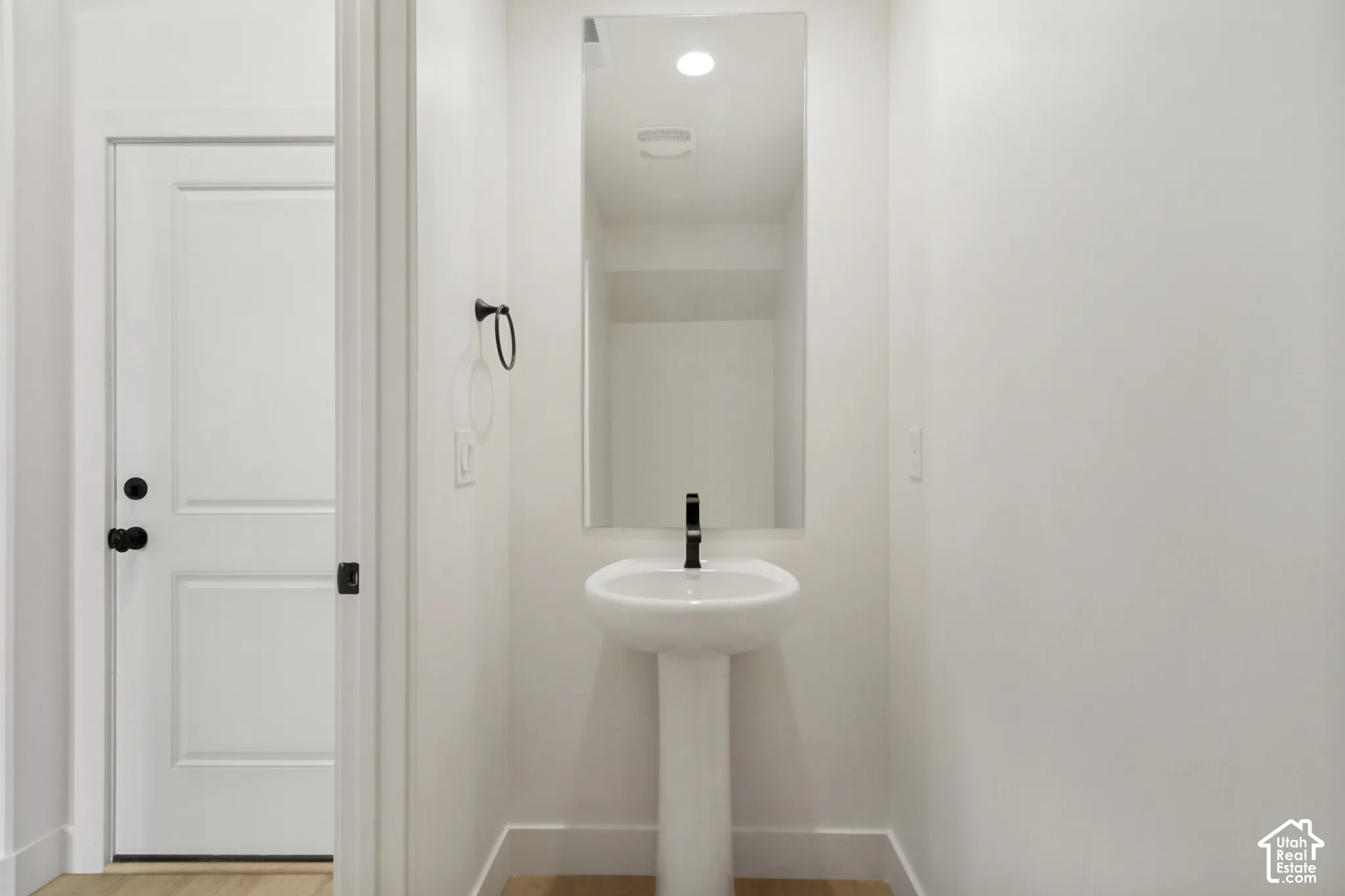 Pedestal sink featuring a matte black faucet, wall-mounted mirror, matte black towel ring, and solid-core door with matte black hardware