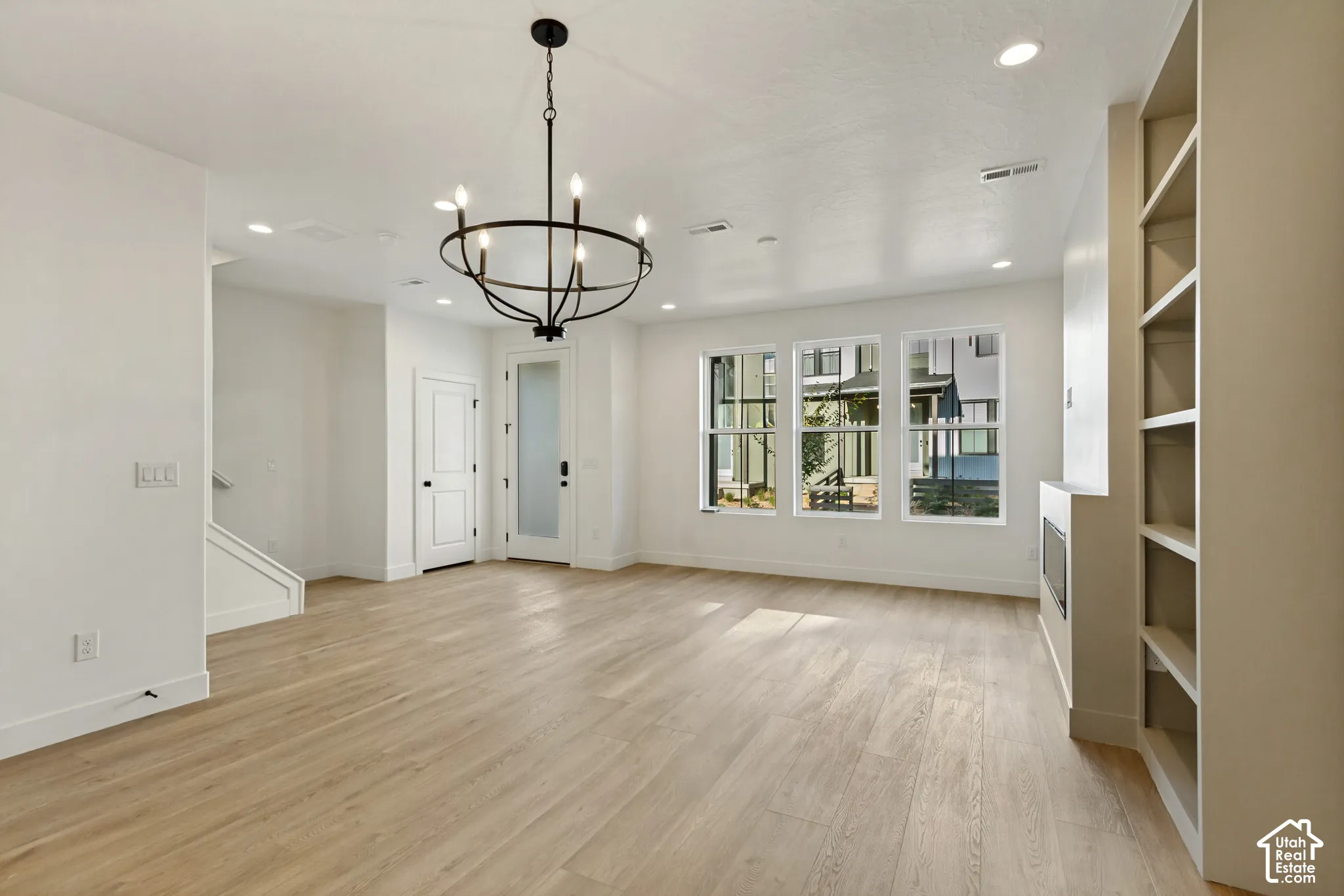 Open-concept interior featuring wood-finish flooring, a contemporary circular chandelier, built-in shelving, a recessed fireplace, and large windows