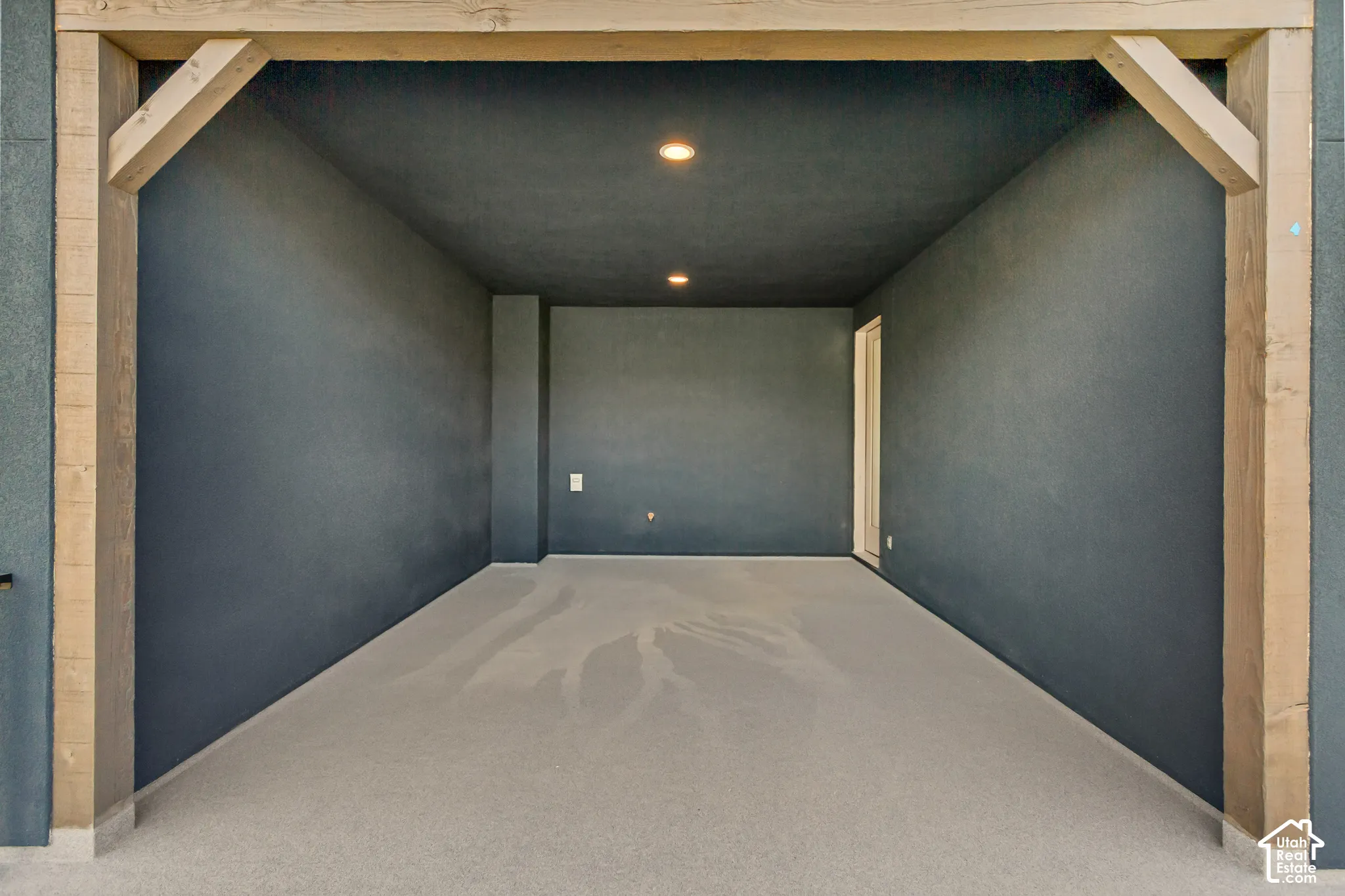 Covered outdoor space featuring exposed timber support beams, recessed lighting, and a neutral-toned concrete surface
