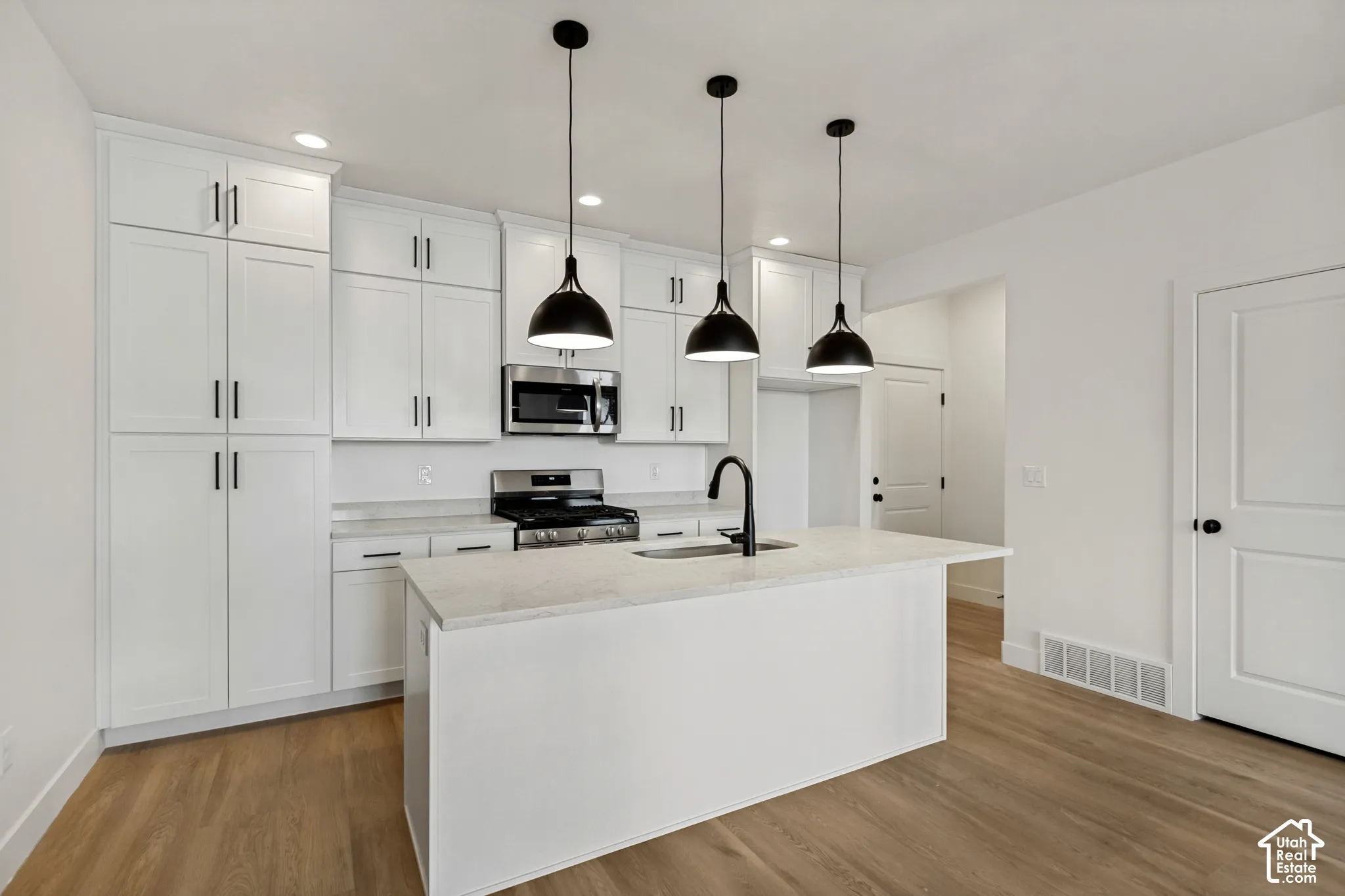 Kitchen featuring white cabinetry with matte black hardware, stone-finish countertops, stainless steel appliance package, a central island with a high-arch faucet, and three pendant lights