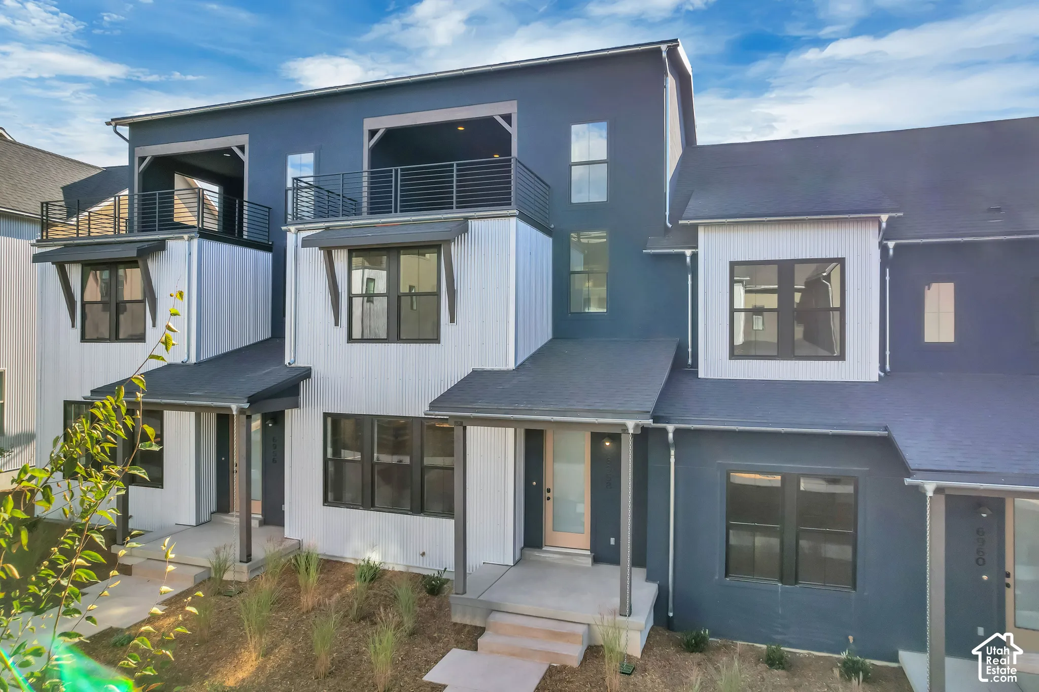 Multi-level exterior featuring vertical siding, charcoal-toned stucco, dual upper-level balconies with metal railings, and covered entryways