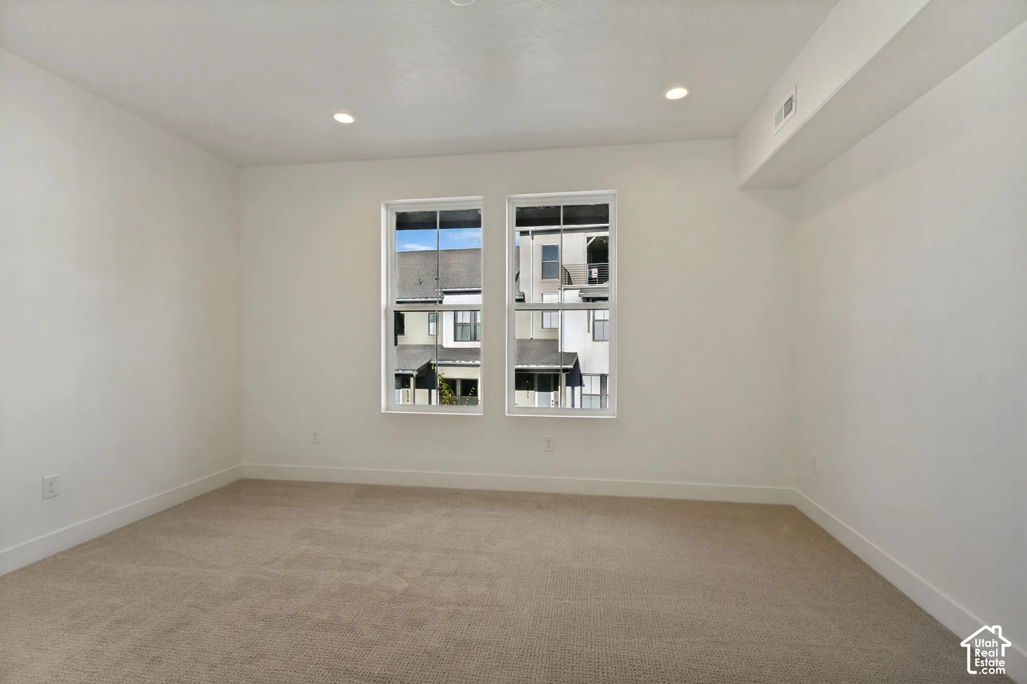 Neutral interior room featuring neutral carpeting, recessed ceiling lighting, and dual grid-pattern windows