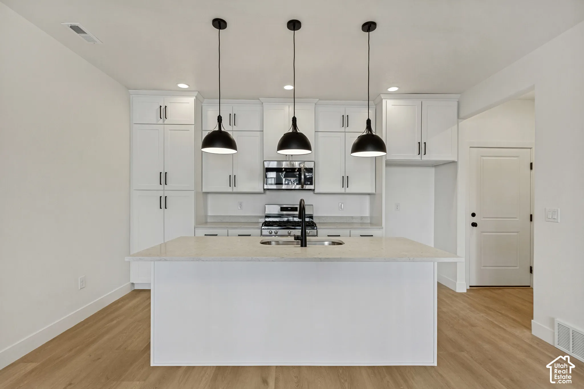 Kitchen featuring white shaker-style cabinetry, quartz countertops, a central island with an undermount sink, matte black pendant lighting, and wood-finish flooring