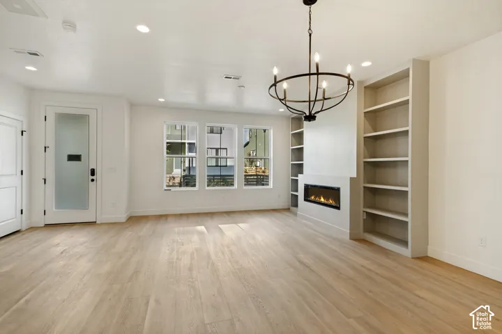 Living area featuring wood-finish flooring, a wall-mounted electric fireplace, built-in floor-to-ceiling shelving, recessed lighting, and a metal candelabra chandelier