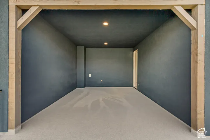 Covered outdoor space featuring exposed timber support beams, recessed lighting, and a neutral-toned concrete surface