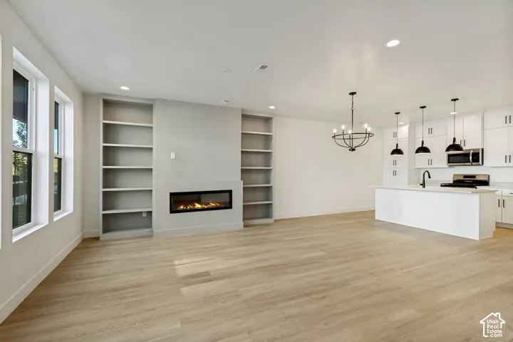 Open floor plan featuring wood-finish flooring, recessed lighting, horizontal built-in fireplace, custom floor-to-ceiling shelving, and kitchen with a central island