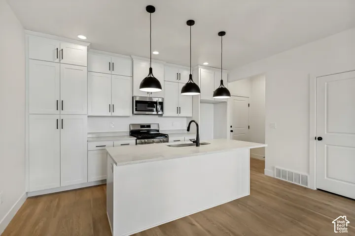 Kitchen featuring white cabinetry with matte black hardware, stone-finish countertops, stainless steel appliance package, a central island with a high-arch faucet, and three pendant lights