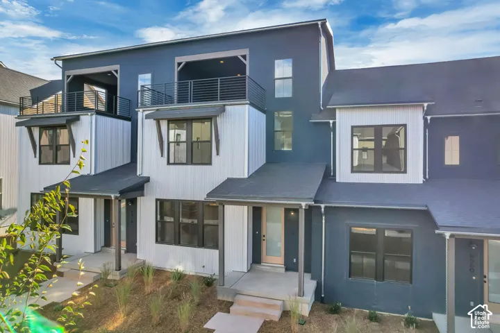 Multi-level exterior featuring vertical siding, charcoal-toned stucco, dual upper-level balconies with metal railings, and covered entryways