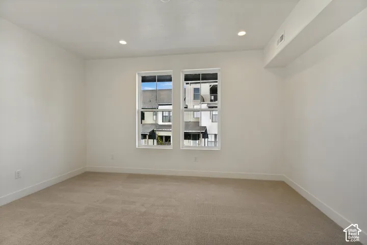 Neutral interior room featuring neutral carpeting, recessed ceiling lighting, and dual grid-pattern windows