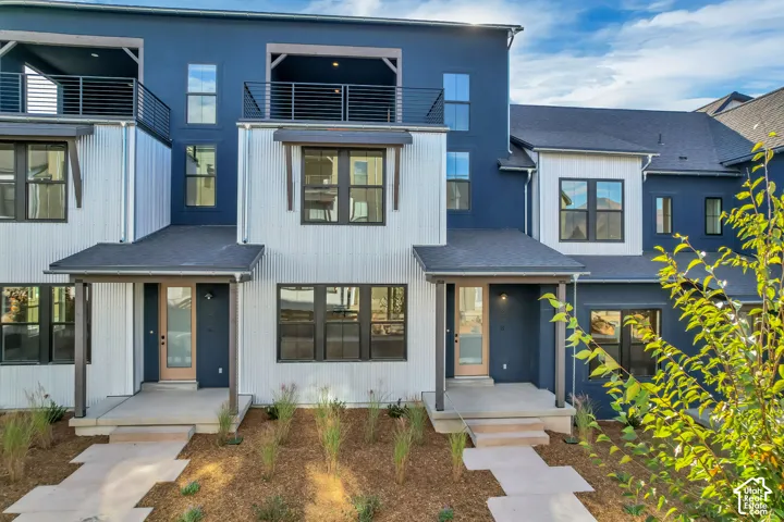 Multi-level facade featuring contrasting blue and white metal siding, upper-level balconies with cable railings, and concrete entry porches