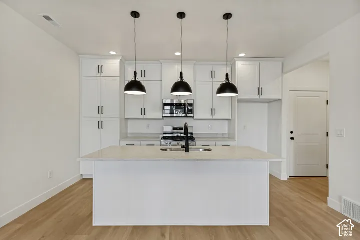 Kitchen featuring white shaker-style cabinetry, quartz countertops, a central island with an undermount sink, matte black pendant lighting, and wood-finish flooring