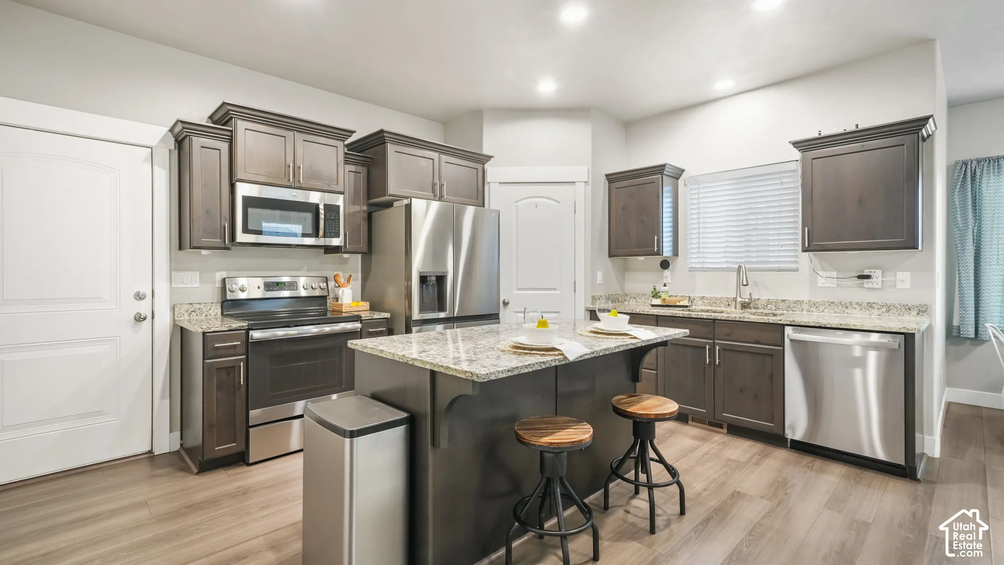 Kitchen featuring stained wood cabinetry, granite countertops, stainless steel appliances, a central island, and wood-finish LVP flooring