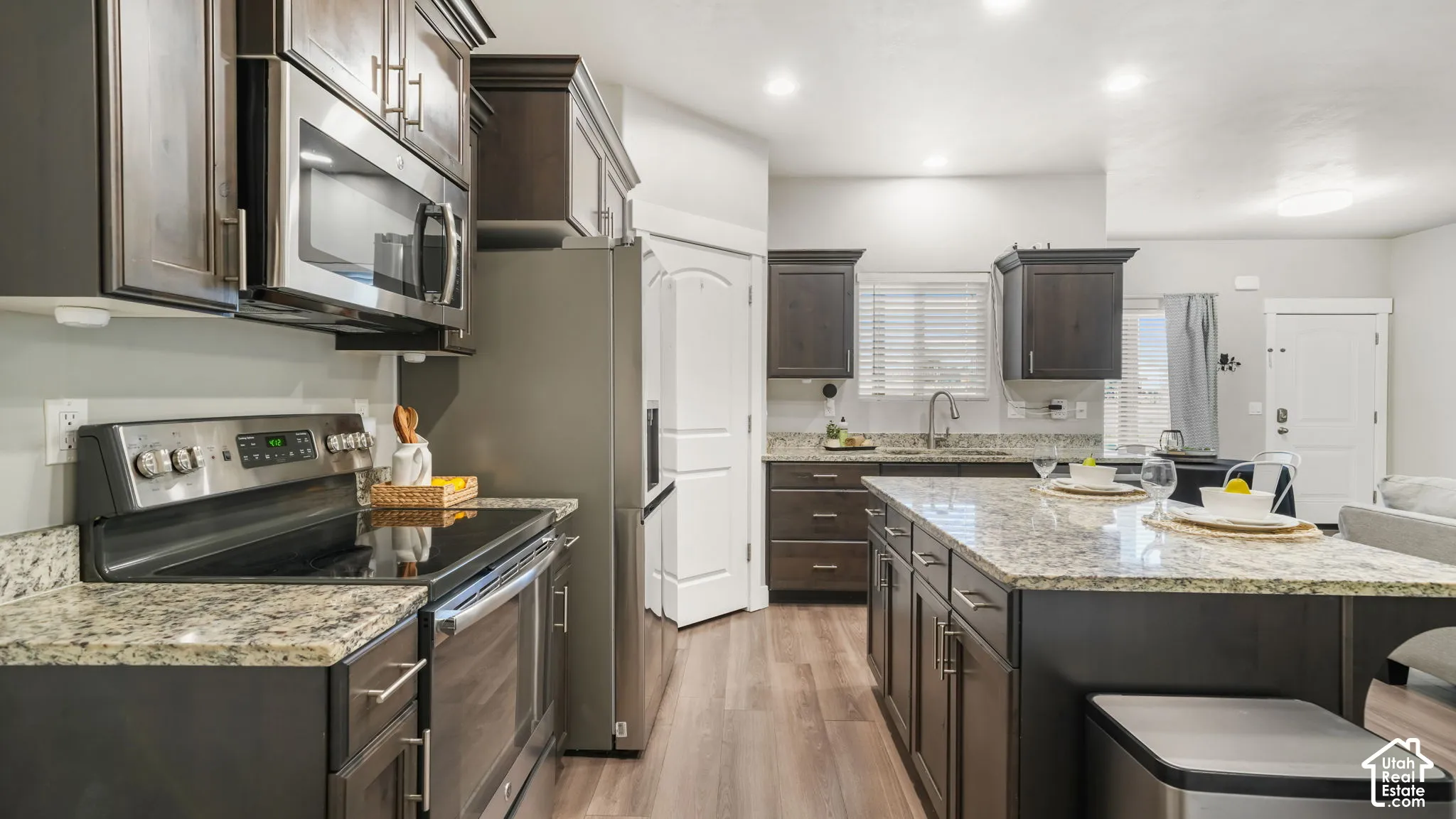 Kitchen featuring dark-finish cabinetry, granite countertops, a large center island, stainless steel appliances, and laminate flooring