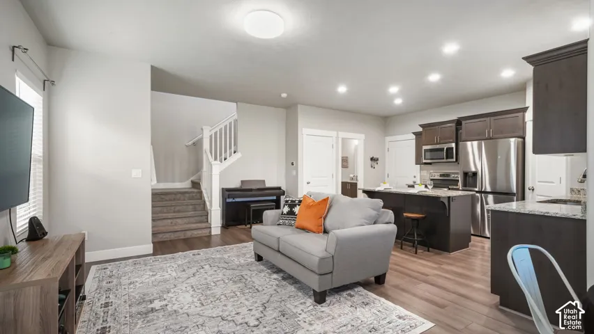 Open-concept layout featuring wood-finish laminate flooring, dark cabinetry, recessed lighting, and a kitchen island with granite countertops