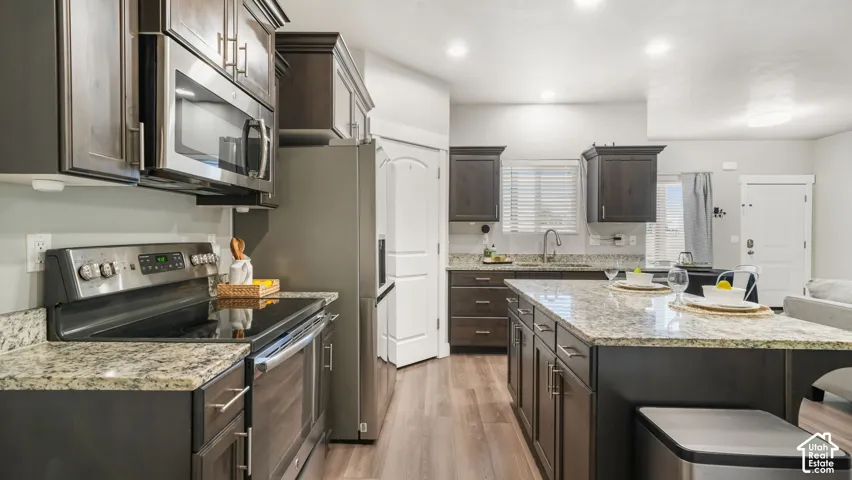 Kitchen featuring dark-finish cabinetry, granite countertops, a large center island, stainless steel appliances, and laminate flooring