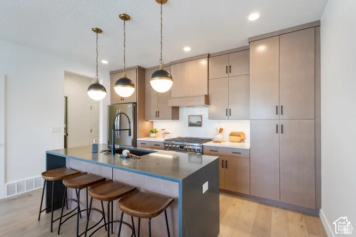 Kitchen featuring custom flat-panel cabinetry, a central island with a solid surface countertop, matte black fixtures, three glass-globe pendant lights, and wood-finish flooring