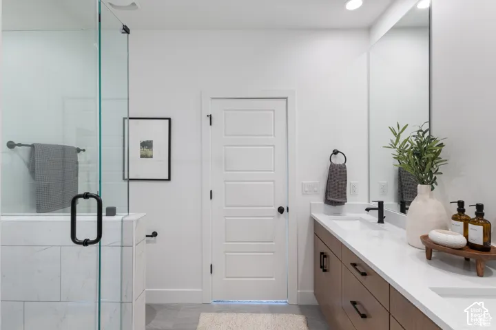 Bathroom featuring a glass-enclosed shower with tiled surround, wood-finish vanity with dual undermount sinks, quartz countertop, and matte black hardware