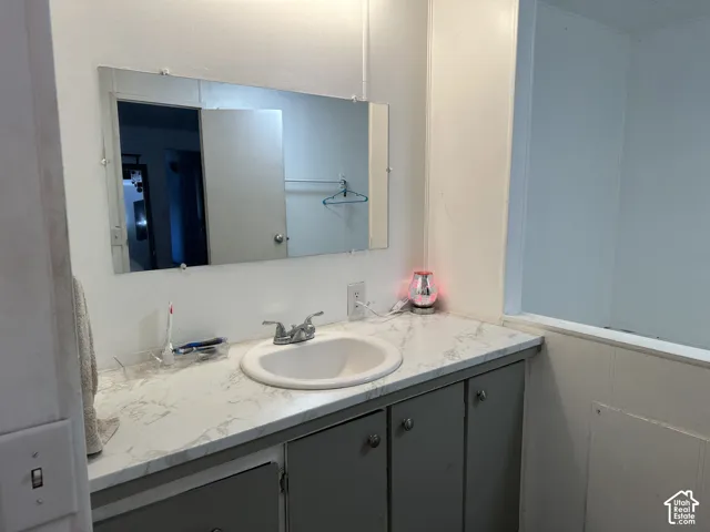 Bathroom vanity featuring a stone-patterned countertop, drop-in basin with a dual-handle faucet, grey cabinetry, and a wall-mounted mirror