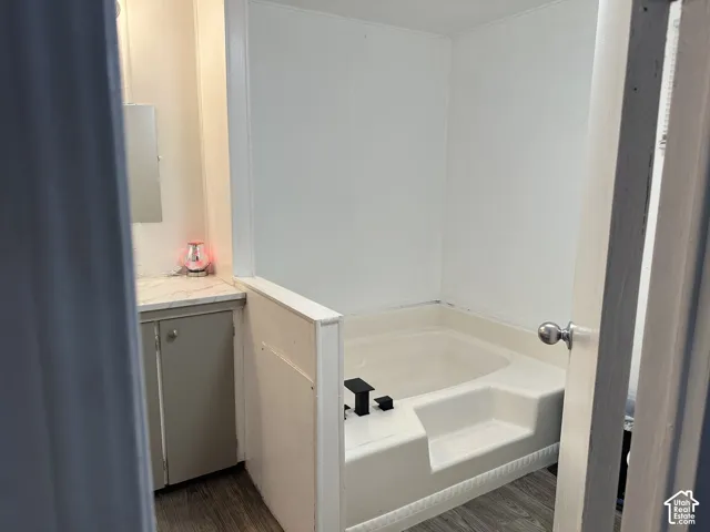 Bathroom featuring a deep-soaking tub, stone-patterned vanity countertop, cabinetry with neutral-finish doors, matte black faucet hardware, and wood-finish flooring