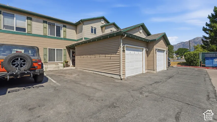 Exterior facade featuring horizontal vinyl siding, dual garage doors, asphalt paving, and gable rooflines set against a mountain backdrop