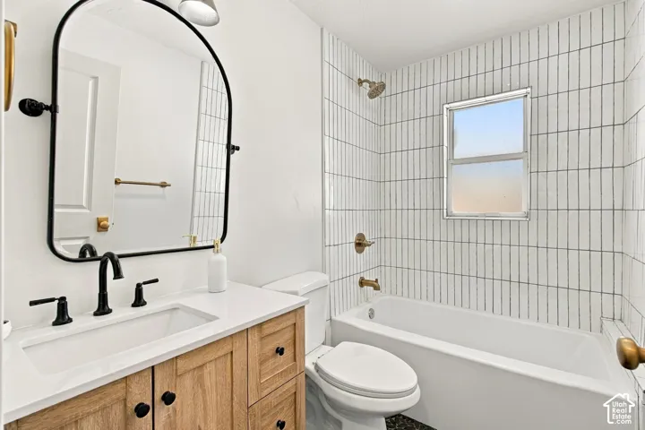 Bathroom featuring a wood-finish vanity with a stone countertop, arch-shaped vanity mirror, matte black fixtures, and vertical tile surround in the shower area