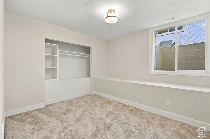 Neutral-toned interior featuring wall-to-wall carpeting, recessed built-in shelving with integrated closet rod, a sliding window with exterior window well, and a flush-mount drum ceiling light