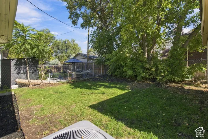 Backyard featuring a grass lawn, mature trees, chain-link fencing, and dark mulch garden beds