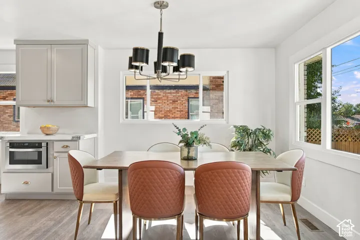 Dining area featuring light-toned cabinetry, built-in stainless steel microwave, multi-arm chandelier, and wood-finish flooring
