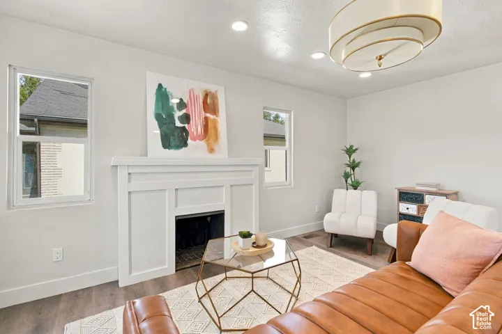 Wood-finish flooring, white fireplace mantel with recessed hearth, dual windows, and multi-tier drum-style light fixture