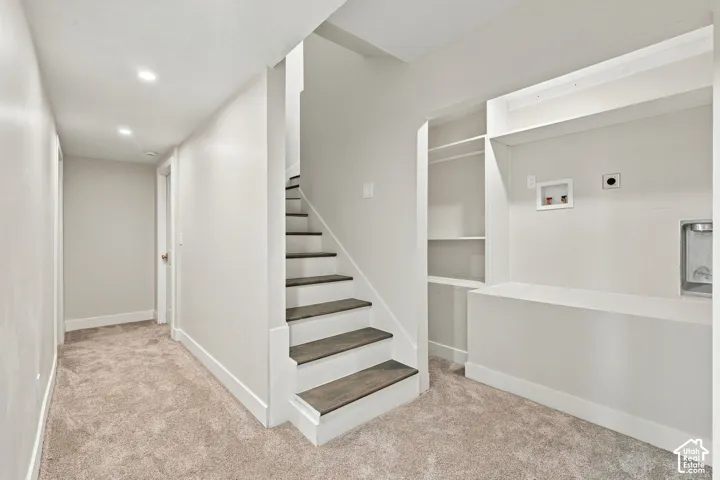 Staircase featuring wood-finish treads and white risers, recessed lighting, wall-integrated laundry hookups, and built-in shelving