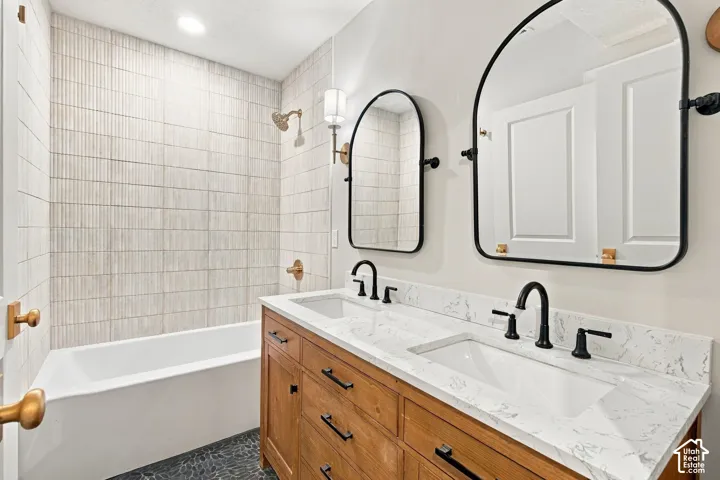 Double vanity featuring a light wood-finish cabinet, stone-finish countertop, dual rectangular undermount sinks, and matte black fixtures