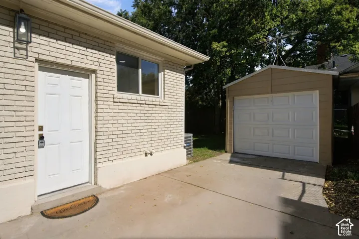 Light-colored brick exterior featuring a white paneled door with wall-mounted lantern lighting, a detached garage with a sectional door, and a concrete driveway