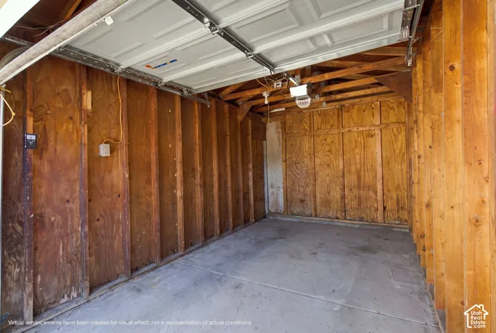 Garage interior featuring exposed wood-stud framing, plywood wall paneling, concrete flooring, and an overhead sectional door